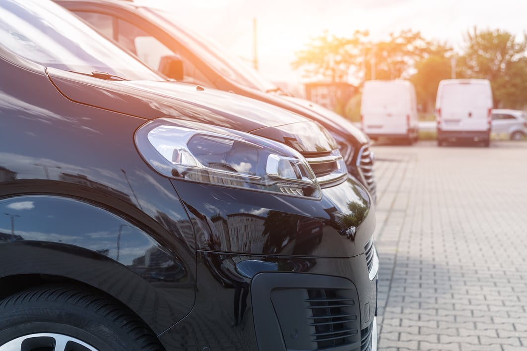 Close-up Detail Headlight View of Many Modern Luxury Black Vans Parked in Row at Car Sale Rental Leasing Dealer against Sunset. Commericial Trasfer Cargo Transportation Company Fleet. Vip Charter